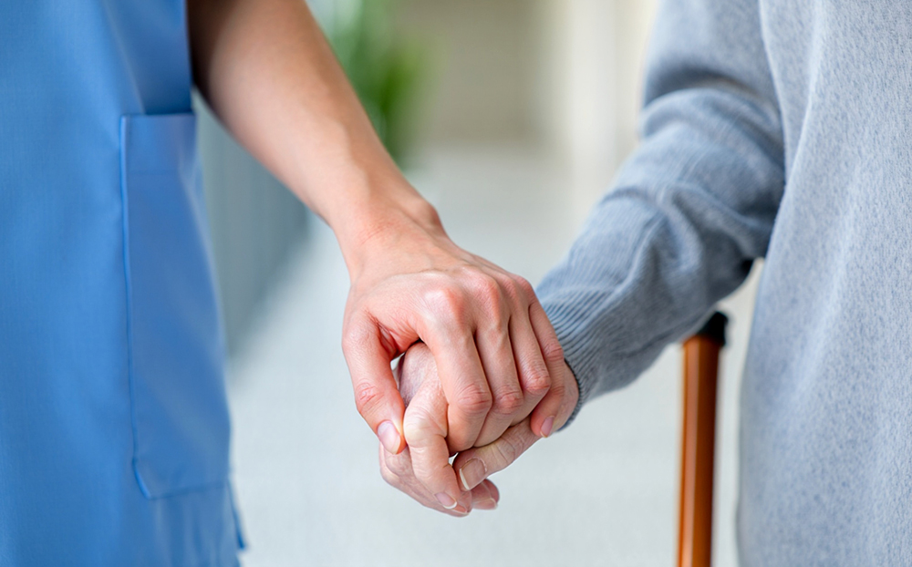Image of care sector worker holding hand of elderly resident